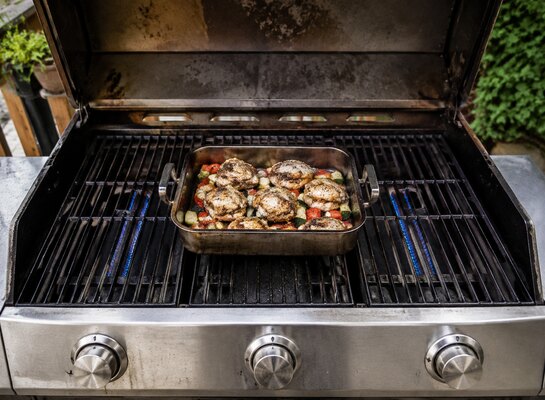 Plat placé au centre d’un barbecue à gaz avec les brûleurs latéraux allumés et le brûleur central éteint