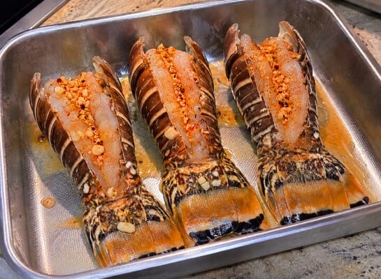 Trois queues de langouste ouvertes et nappées de beurre à l’ail et au Tokyo Fire avant leur cuisson au four